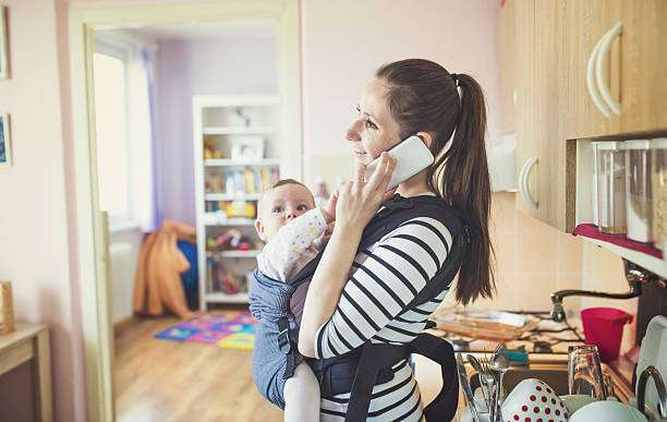 A young mother makes a phone call while using a baby carriers.