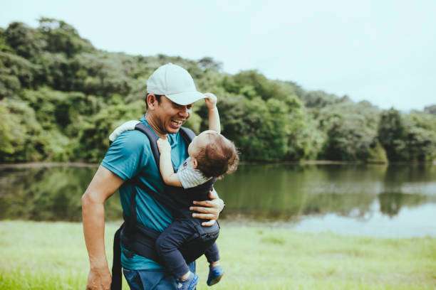 A father carries his child in a baby carrier while playing in the forest.