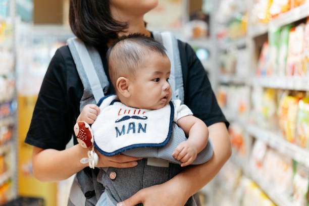 Baby strolls through the supermarket in a baby carrier carried by mom.