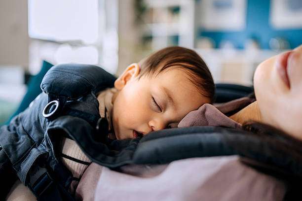 Cute little baby girl sleeping with her mother in baby carrier