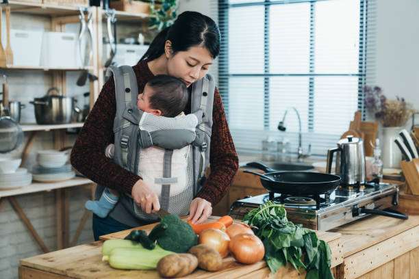 Mother using phone while her baby girl in sleeping on her chest in baby carrier