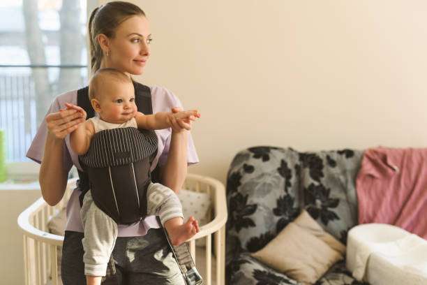 Mother using phone while her baby girl in sleeping on her chest in baby carrier