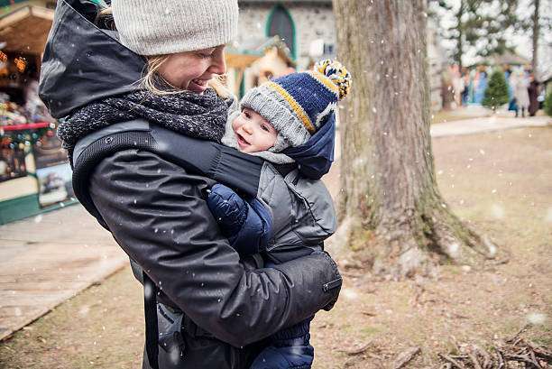 In the snow, a mother and baby embrace each other in a baby carrier.