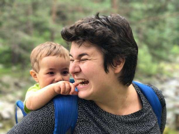 The baby smiles with his mother in the baby carrier.