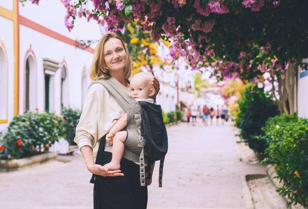 Woman working on a laptop while holding baby carrier