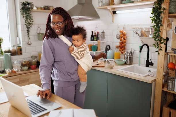 Woman working on a laptop while holding baby carrier