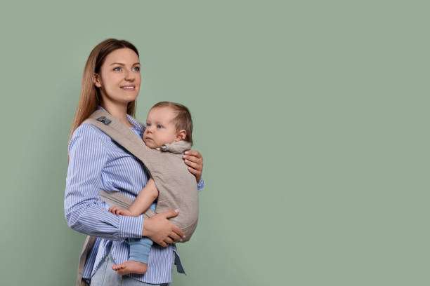 Mother holding her child in sling (baby carrier) on olive background.