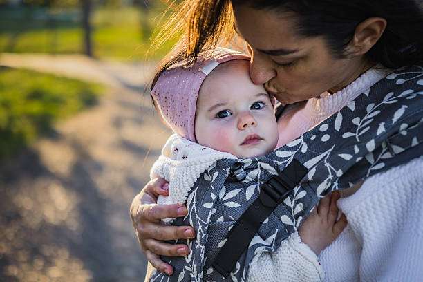 Mother is carrying her daughter in baby carrier during a walk.
