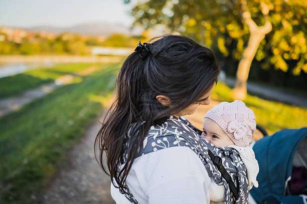 Mother is carrying her daughter in baby carrier during a walk.