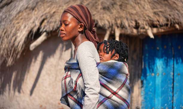 Mother holds baby son on hilltop above sea at sunset, baby carrier