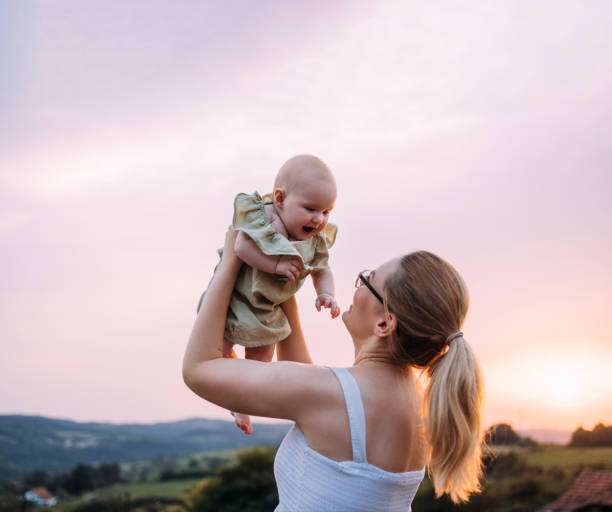 woman standing in her backyard, holding her newborn baby up in the air.have their babies in baby carrier