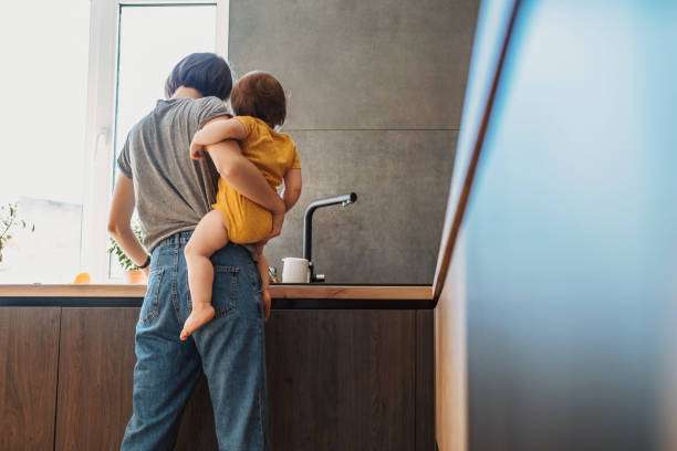Mid adult man working using laptop and taking care baby son at home.baby carrier
