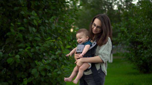 Happy woman looking to distance while holding and carrying it in a baby carrier in a park