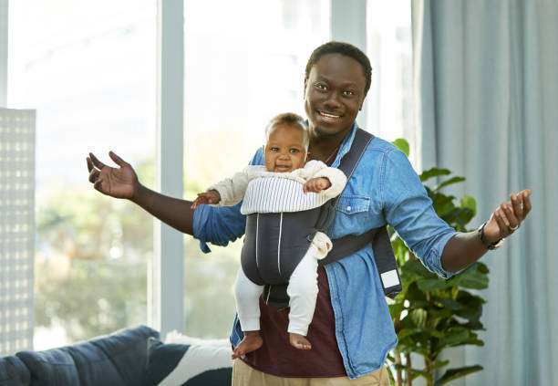 Mid adult man working using laptop and taking care baby son at home.baby carrier