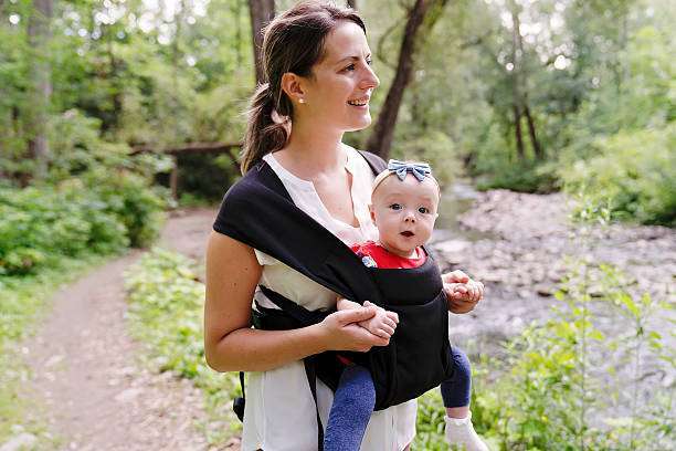 Happy woman looking to distance while holding and carrying it in a baby carrier in a park